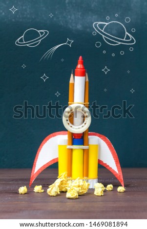 Back to school concept. Rocket cut from paper and pencils on blackboard background.
