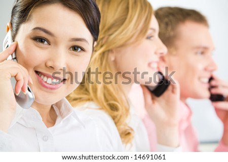 Face of smiling businesswoman making phone call and looking at camera with smile on background of two phoning people