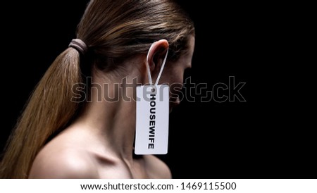Lady with housewife label on ear against dark background, place of women, sexism Royalty-Free Stock Photo #1469115500