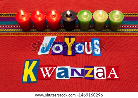 JOYOUS KWANZAA text word collage typography, with seven candles and multi colored fabric on red woven fabric, African American holiday, horizontal aspect