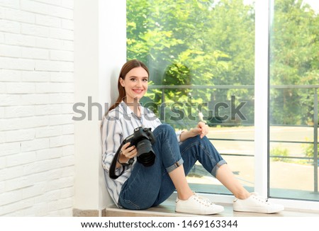 Professional photographer with modern camera sitting near window indoors
