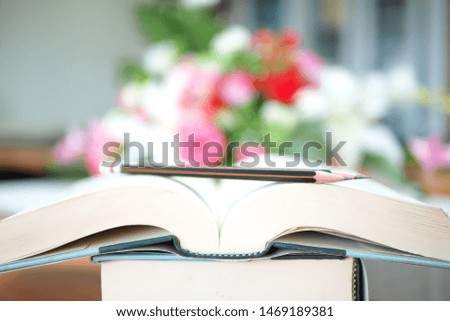 Education concept of books and pencils in selective focused mode. Academic idea picture of big open book and some pencils on it with the colorful blurry background of flowers on a back in a study room