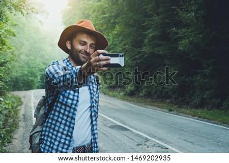 Travel blogger man taking a photo or selfie on the background of a foggy automobile road. Writes a blog on a smartphone.
