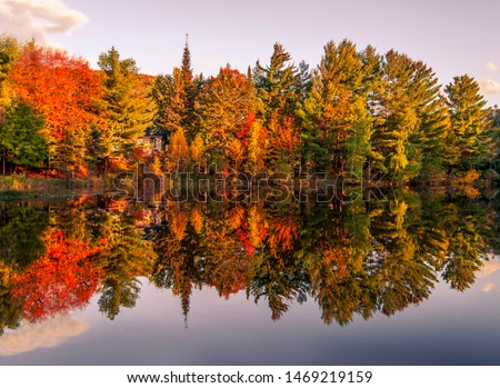 Landscape photo of a colorful forest reflecting on a lake's calm waters. Beautiful fall foliage - yellow, red and orange. Shot in Mont-Tremblant, Quebec, Canada. 