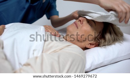 Sick woman suffering from fever and ravings, nurse putting compress on forehead