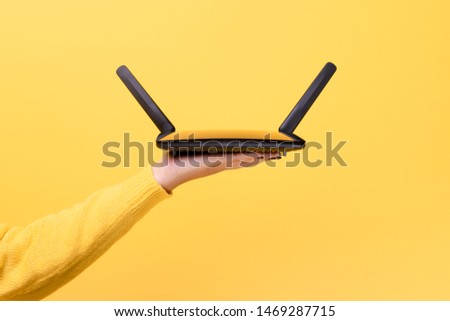 black wifi router on female hand over yellow background Royalty-Free Stock Photo #1469287715