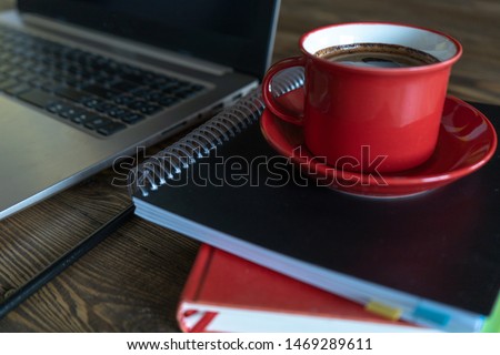 Red cup of fresh morning coffee on the notobook on wooden table in the office. Top-side view. Close-up