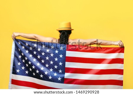 patriotic woman with American flag over yellow background. USA Independence day, 4th July. Freedom concept, view from the back.