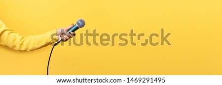 hand holding microphone over yellow background, panoramic mock up image Royalty-Free Stock Photo #1469291495