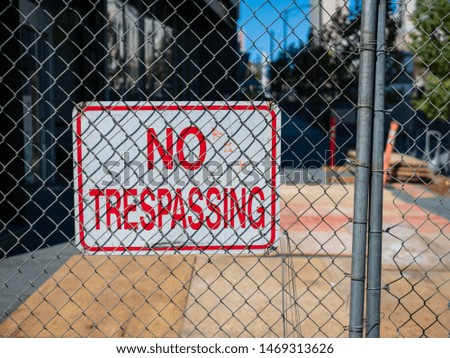 No trespassing sign behind fence wire in front of an urban construction