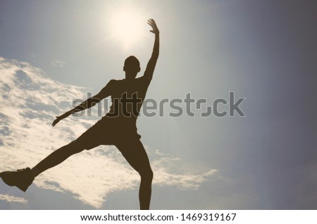 A young man tries to reach the sun, he jumps and raises his hand up, silhouette.                                                               