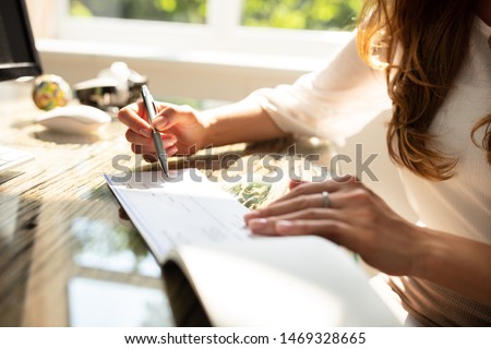 Businesswoman's Hand Signing Cheque On Wooden Desk Royalty-Free Stock Photo #1469328665
