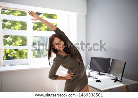 Smiling Young Businesswoman Doing Stretching Exercise In Office