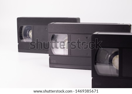 Three old black video cassettes stand in a row one after another on a white background.