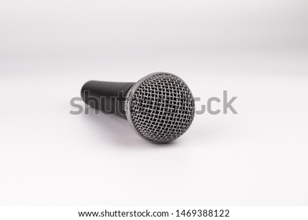 On a white background lies a microphone. The microphone in two colors is gray and black. The microphone head is covered with a net.