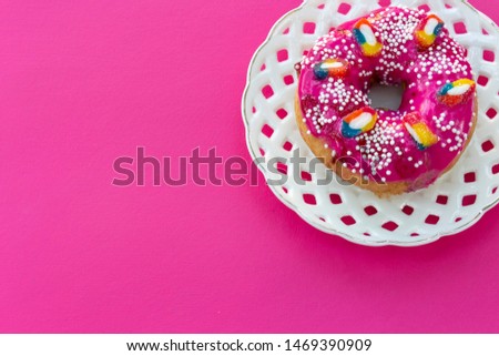 Pink glazed donut on a white openwork plate on a bright pink background with place for text