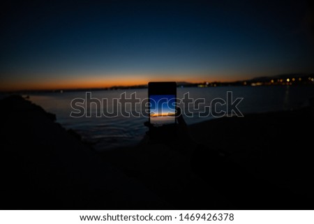 human hand holding a phone taking a picture of a sunset view over the sea