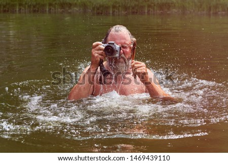 Taking pictures using waterproof camera by white man, who is standing in river and watching into his camera.