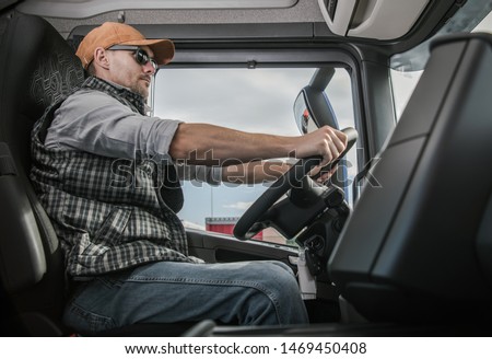 Trucker on the Route to Destination. Cargo Shipping Theme. Caucasian Semi Truck Driver Inside Vehicle Cabin. Royalty-Free Stock Photo #1469450408