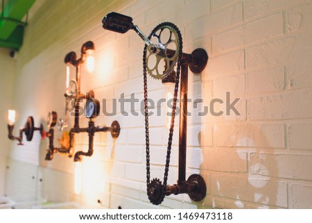 Steampunk architectural style design element of interior. Lamp bulbs fixed on iron industrial gear cogwheels sprocket lighting illuminated equipment hanging indoors.