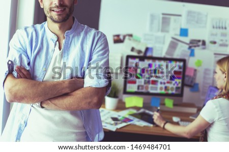 Portrait of young designer in front of laptop and computer while working. Assistant using her mobile at background.