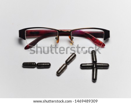 Eye glasses with plus and minus sign made from capsules isolated on white background. Eyesight correction concept
