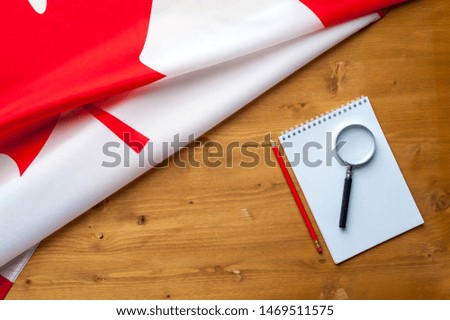 Top view flag of Canada notepad pencil and magnifier lie on a wooden table. Place for advertising. Concept of searching for real estate information in the country