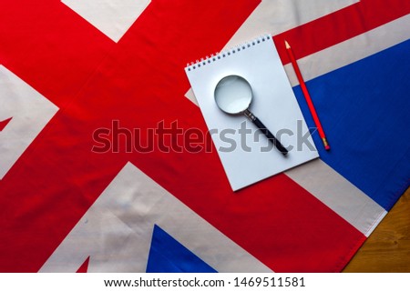 Top view flag of United Kingdom with notepad, pencil and magnifier lie on a wooden table. The concept of finding information and work in the country. Advertising space