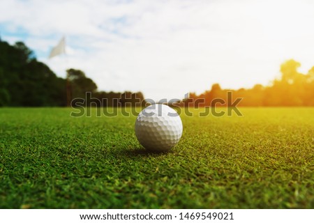 golf ball on green grass with hole and sunlight