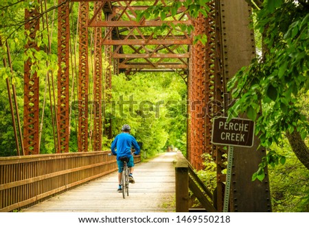 Man bicyclist riding under old railroad bridge in Missouri State Park in late afternoon Royalty-Free Stock Photo #1469550218