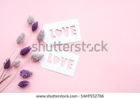 White gift tag with inscription love, on a pink background, decorated with  dried flowers of gently purple color.
