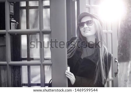 Beautiful young girl in a phone booth. The girl is talking on the phone from the payphone. English telephone booth in the street and a woman talking on the phone.
