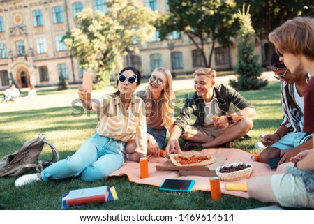 Selfie mood. Students wearing big glasses taking selfies sitting on the grass lawn during their picnic near the university.