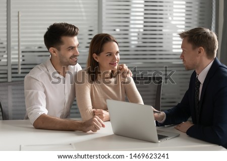 Happy millennial couple talk with male real estate agent or broker in office buying first house together, smiling young husband and wife speak visit banker think of taking loan or mortgage from bank Royalty-Free Stock Photo #1469623241