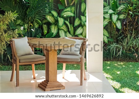 Patio with two wooden chairs and table in the garden full of green tropic plants