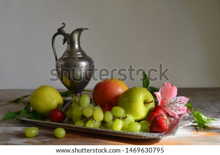 Metal jug on a metal tray with grapes and apples and strawberries