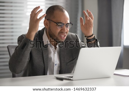 Mad male employee in glasses feel nervous having computer software problems or virus attack, angry man worker wearing spectacles use laptop get annoyed bothered by slow internet connection in office