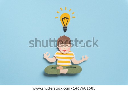 Smiling young man sitting in lotus pose and meditating. Teen with lightbulb concentrating on new idea for solution of important question. Hand cut illustration from paper