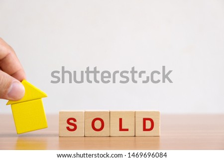 Property investment and house mortgage financial concept. Hands holding wooden house and wood cube block with SOLD word.