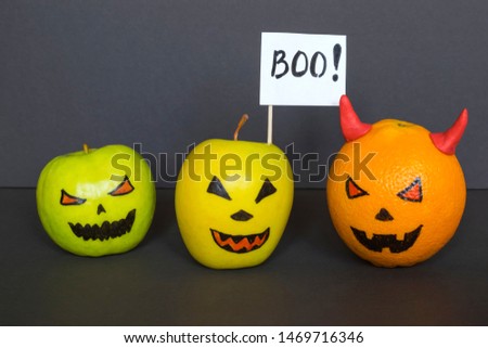 Orange and apples with scary faces as Halloween pumpkins on the dark background. 