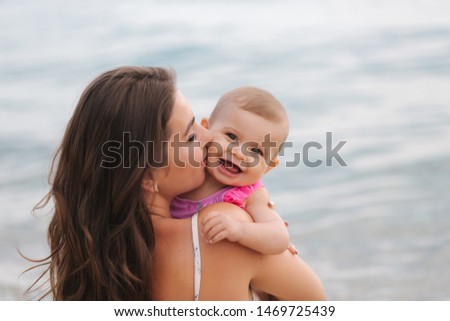 Mom kiss her little daughter on the beach. Backgound of sea