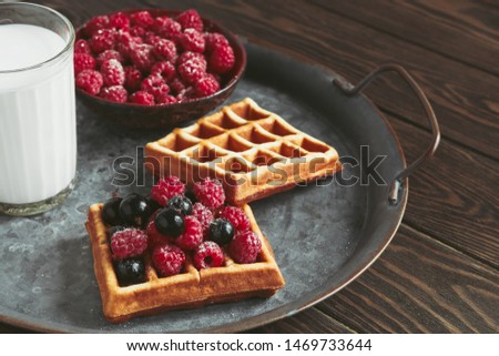 homemade waffles filled with fresh berries and a glass of milk lie on a wooden table