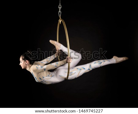 Portrait of a gorgeous young, flexible girl, of European appearance, an air acrobat, in a light suit performing circus tricks on an air ring, on a black background. Close-up studio shot.