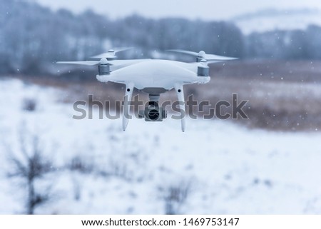 Hovering drone taking pictures of wild nature. Cold winter weather. Cloudy day with falling snow.