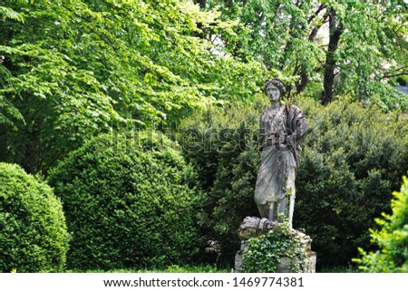 Grey statue surrounded by green plants and trees