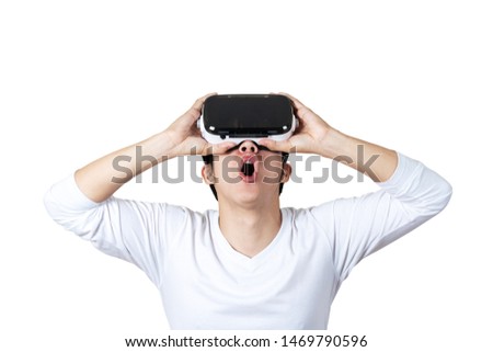 Young asian man in casual white outfit holding or wearing VR glasses by hands looking up above 360 degree feeling excited and amazed on isolated white background. Virtual reality experience concept.