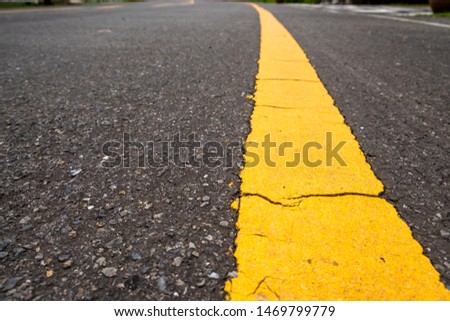 Perspective view of bright yellow traffic dividing line on black asphalt road.