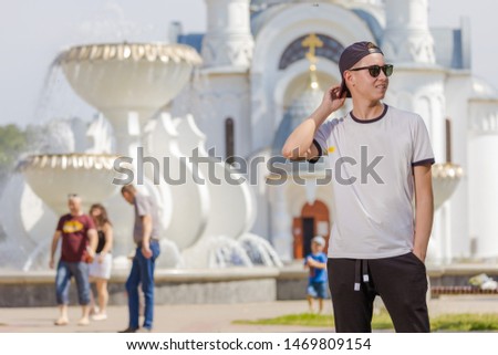 A man stands posing against the white church on a sunny day