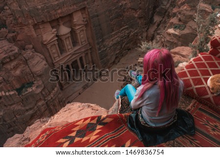 top view travel photography of sitting girl with pink hair back to camera on edge of high cliff looking on Petra treasure ancient architecture building Jordan national heritage site destination 