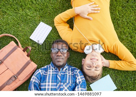 Above view portrait of two students lying on green grass and looking at camera, copy space